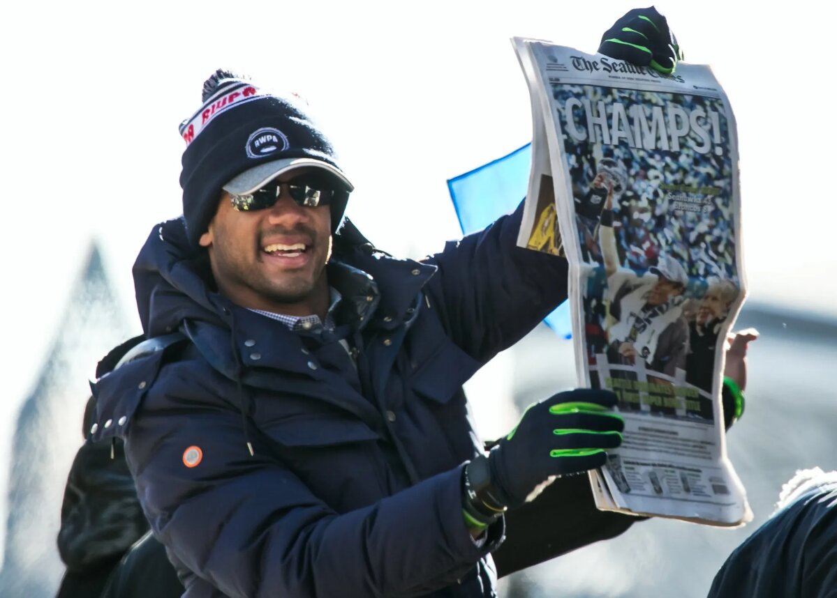 Seahawks quarterback Russell Wilson holds up a copy of The Seattle Times featuring the Super Bowl XLVIII winners for the crowd to see during the Seahawks Super Bowl parade along Fourth Avenue in downtown Seattle. (Marcus Yam / The Seattle Times, 2014)